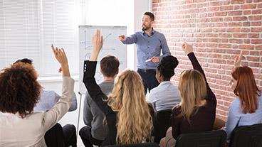 Trainer calling on employees with raised hands in workplace training session.
